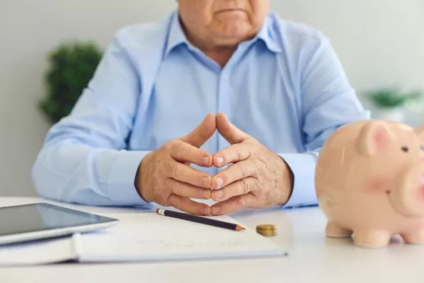 um senhor com as mãos unidas olhando para um cofrinho de porco