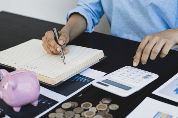 Homem escrevendo em uma agenda e fazendo também cálculos.